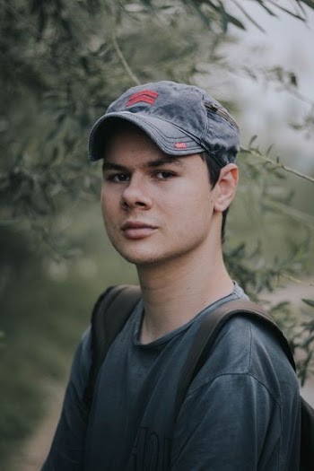 Man in a baseball hat and backpack making eye contact outsite