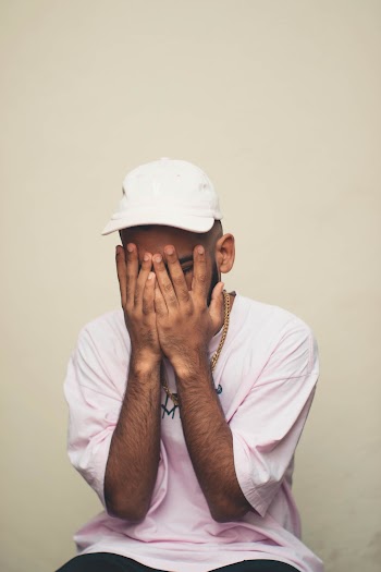 Man in a White Baseball Cap Covering His Face with His Hands