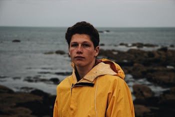 Man in a yellow jacket standing near a water body 
