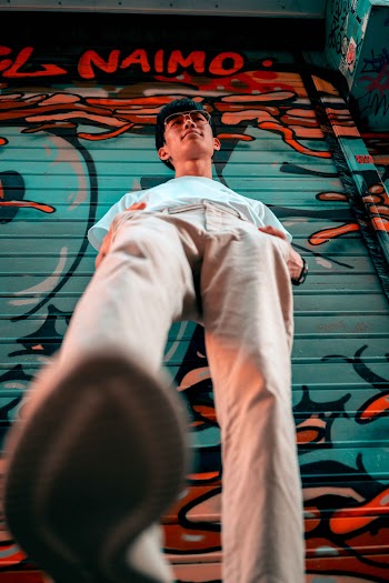 Man in Beige Denim Jeans and White Crew Neck T-shirt Standing in Front of Graffiti Painted Metal Door