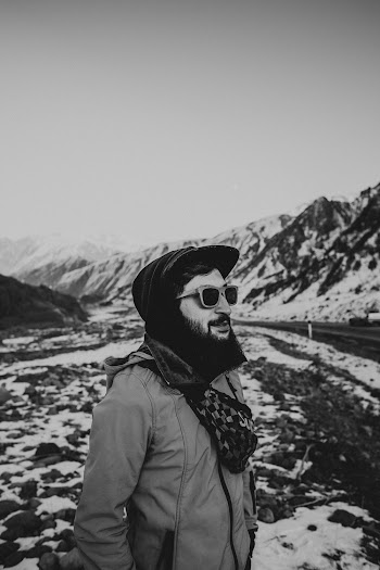 Man in Beige Jacket and Fitted Cap by Snow Covered Mountains