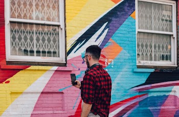 Man in Black and Red Gingham Sport Shirt Holding Smartphone in Front of Wall