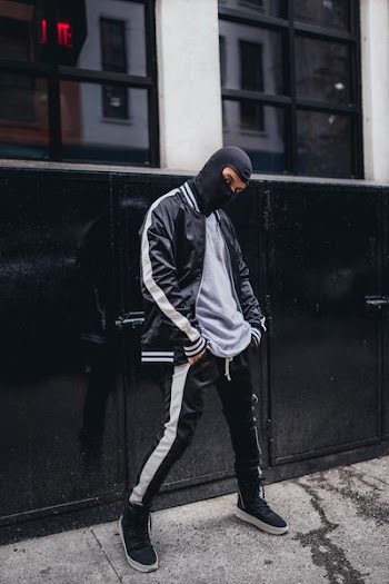 man in black and white letterman jacket wearing balaclava with hands in pocket near black metal gate