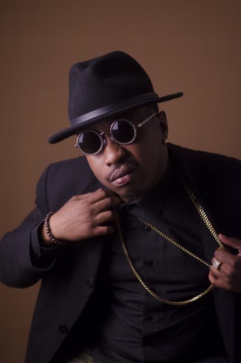 Man in Black Blazer and Black Hat Holding His Gold Necklace
