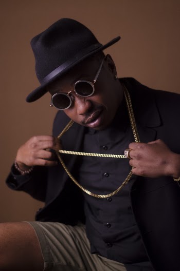 Man in Black Blazer and Brown Short Pulling His Gold Necklace With Both Hands