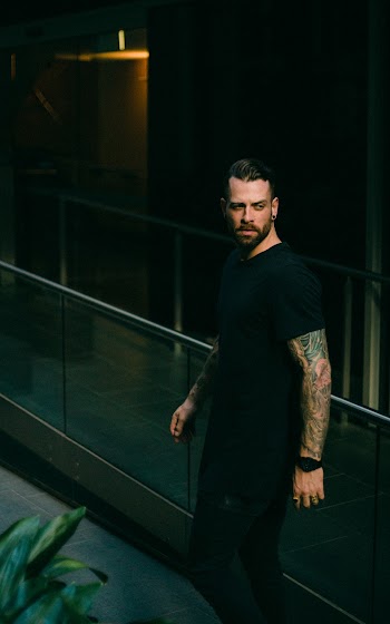 Man in Black Crew-neck Top With Arm Tattoos Looking Over His Shoulder