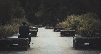 Man in Black Dress Shirt With Blue Denim Shirt Sitting on Black Concrete Bench Near Green Plants