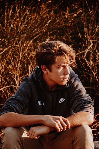 Man in Black Hoodie Jacket Sitting on Brown Grass Field