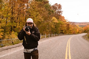 Man in Black Jacket and White Cap Holding Camera