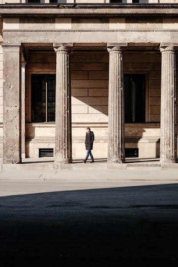 man in black jacket walks on building posts