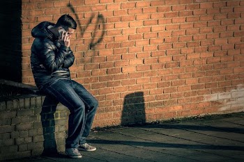 man in black leather jacket sitting on brick wall holding smartphone