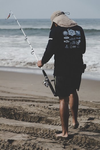 Man in Black Long-sleeved Top Holding White Fishing Rod Near Beach