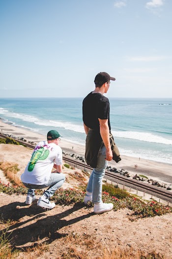 Man in Black Shirt and Blue Jeans Standing on Cliff Facing Ocean