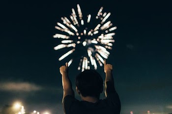 man in black shirt pointing towards brocade fireworks in the skies