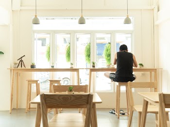 Man in Black Sleeveless Shirt Sitting on Wooden High Chair Beside Wooden Tables Near Window