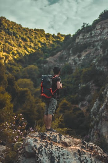 Man in Black T-shirt Carrying a Bag-pack Standing on Cliff
