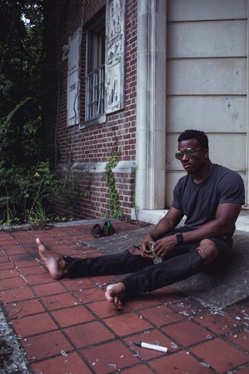 Man in Black T-shirt Wearing Sunglasses While Sitting in Front of Door