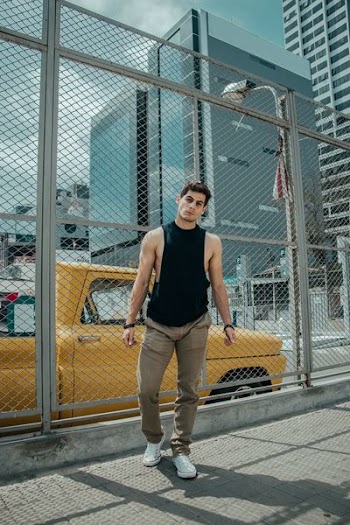 man in black tank top and brown jeans standing beside of wire fence during daytime