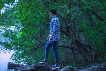 Man in Blue and Black Gingham Button-up Top Standing on Brown Wood Log in Forest
