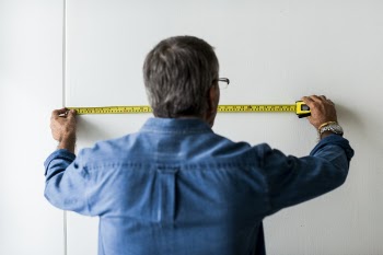 Man In Blue Collared Long Sleeved Shirt Measuring The Wall