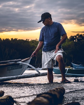 Man in Blue Crew Neck T-shirt and White Shorts Standing Near White Boat during Sunset