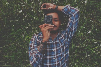 Man in Blue Dress Shirt Holding Camera White Laying on Grass