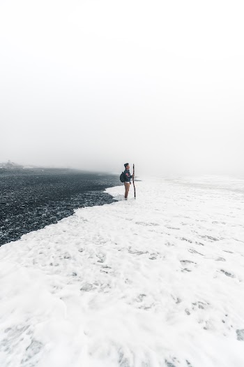 Man in Blue Jacket and Blue Denim Jeans Standing on Snow Covered Ground