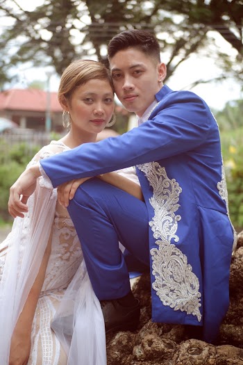 Man in Blue Suit Sitting on Rock in Front of Woman in White Wedding Dress