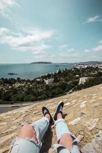 Man in Blue Tattered Jeans Sitting on Top of the Mountain