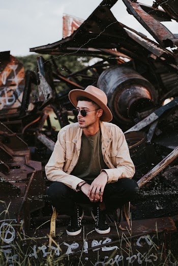 Man in Brown Denim Jacket Sitting Infront of Metal Scraps