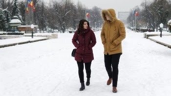 Man in Brown Parka Jacket Walking Beside Woman in Maroon Coat