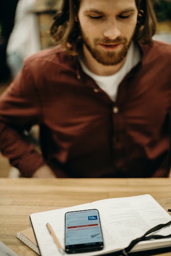 Man in Brown  Shirt Sitting at the Table Near a Smartphone