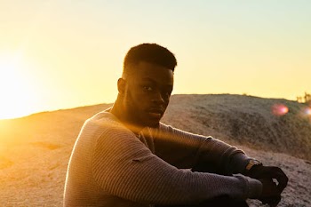 Man in Brown Sweatshirt Sitting Near Cliff at Daytime