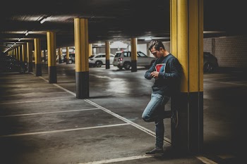Man in Dark-gray Crew-neck Sweater Standing Leaning to Post in Parking Lot