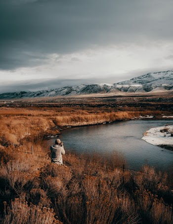 Man in Front of Body of Water Under Cloudy Sky