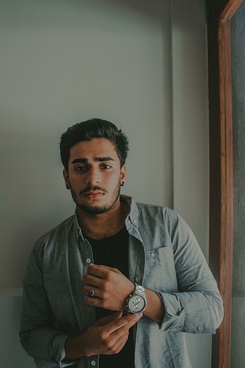 Man in Gray Dress Shirt Standing Beside Wall Touching His Watch