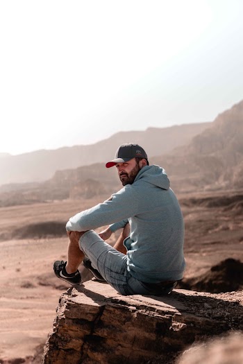 Man in Gray Hoodie and Gray Pants Sitting on Brown Rock
