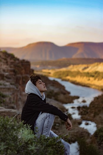 Man in Gray Hoodie Sitting on Cliff