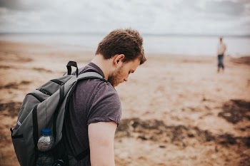 man in gray shirt and backpack beside beach shore during daytime