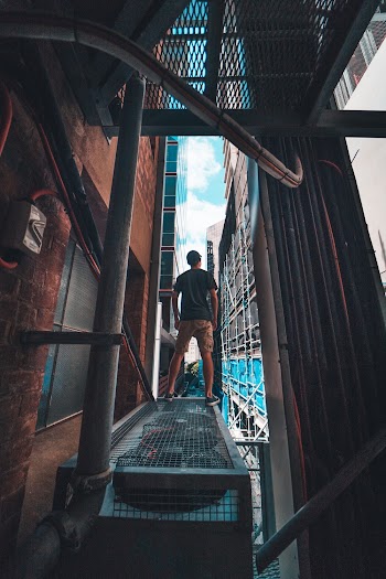 Man in Gray Shirt Standing on Gray Metal Scaffolding