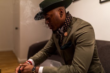 Man in Green Blazer With Cap Sitting on Black Sofa
