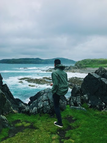 Man In Green Hooded Jacket And Jeans Standing Near Rocks