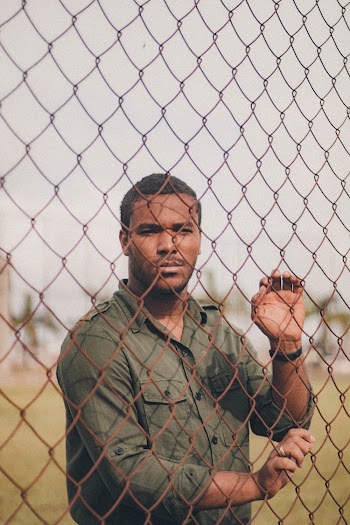 Man in Green Shirt Standing Behind Chain Link Fence
