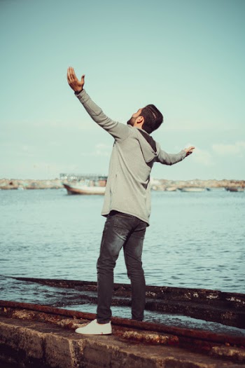 Man In GrEy Hoodie Standing on Grey Pavement Near Sea