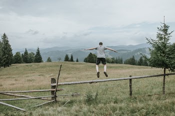 Man in Grey T-shirt Jumping over Brown Fence on Green Field