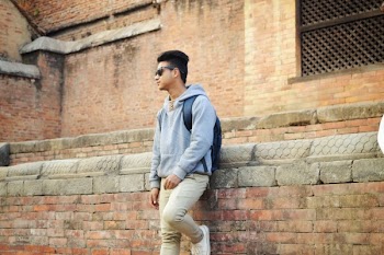Man in Heather-grey Pullover Hoodie and Beige Pants Standing Near Brick Wall