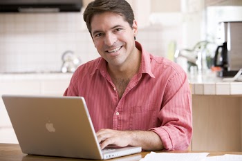 Man in kitchen using laptop smiling