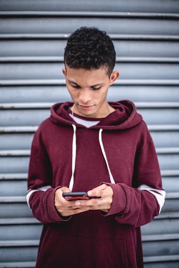 Man in Maroon Hoodie Using Smartphone in Front Roller Shutter