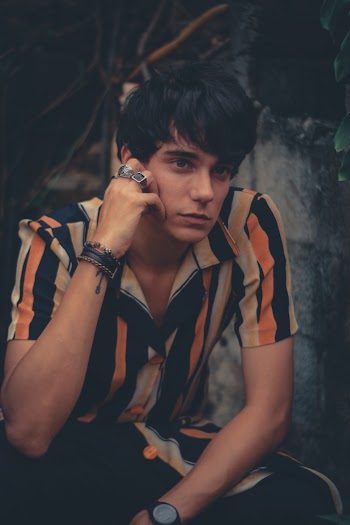 Man in Multicolored Button-down Shirt Sitting Near Grey Concrete Wall