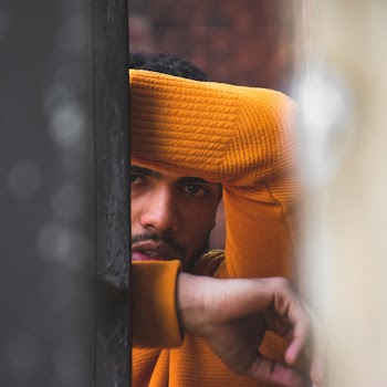 Man In Orange Long Sleeve Shirt Leaning On Wall